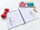Chilli Keepsakes spiral dog memory book open to first and second birthday pages, with space to record milestones and add photos, styled with dog toys and treats.
